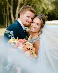 Bride and groom embracing during portrait with flowing light blue veil and colorful garden-style bouquet at outdoor Maryland Eastern Shore wedding.