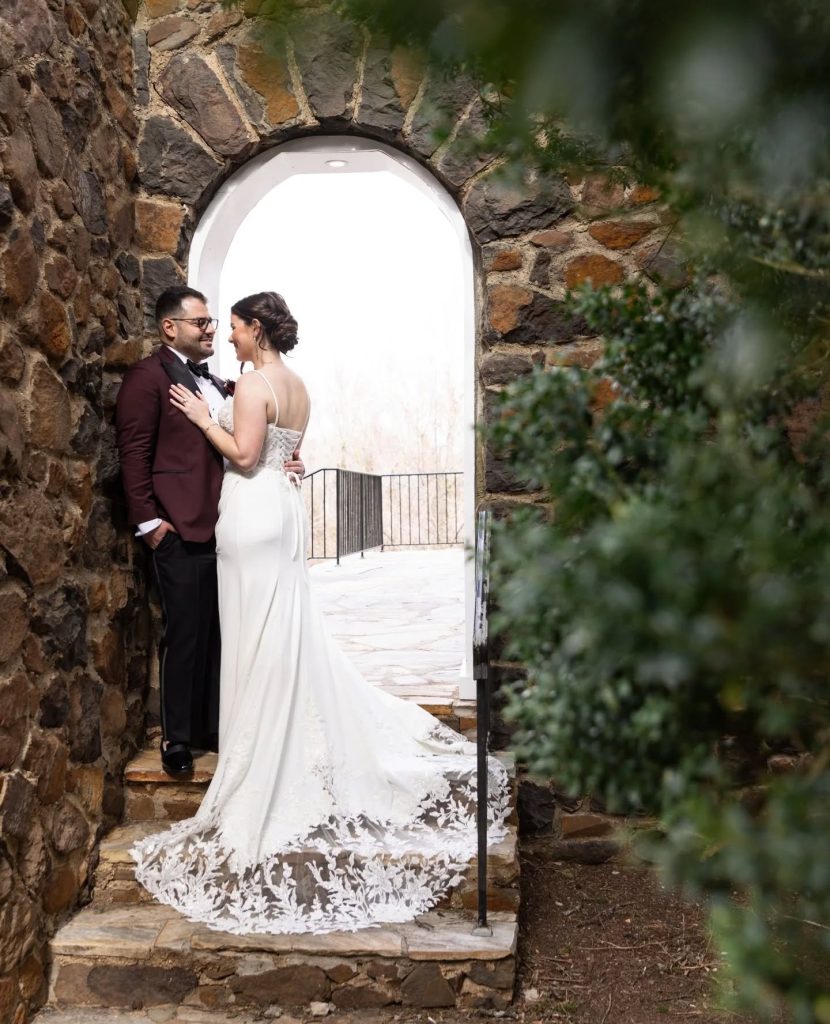 Wedding Couple laughing and talking while leaning about stone wall with arch at their outdoor wedding ceremony
