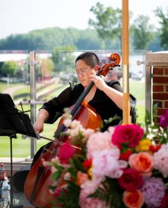 Cellist plays at outdoor golf club wedding with bright pink, coral, and white flowers in the forefront
