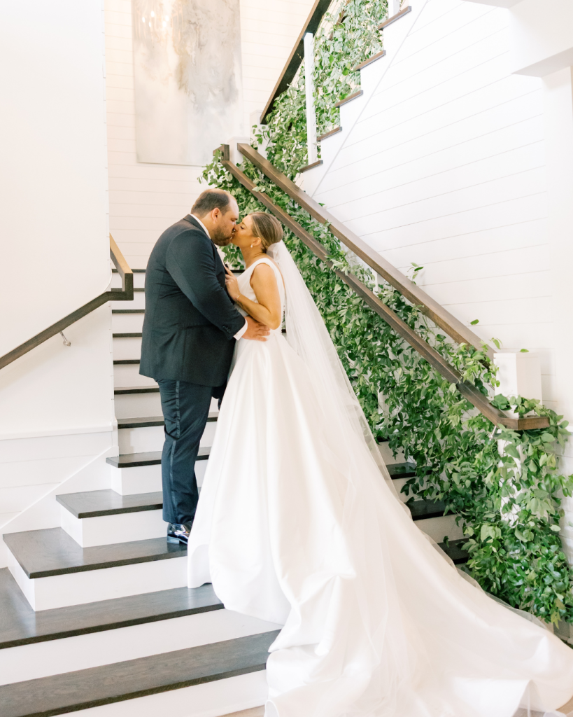 Bride and groom kissing on staircase with greenery during wedding portraits at Bayside Resort Golf Club in Selbyville, Delaware.