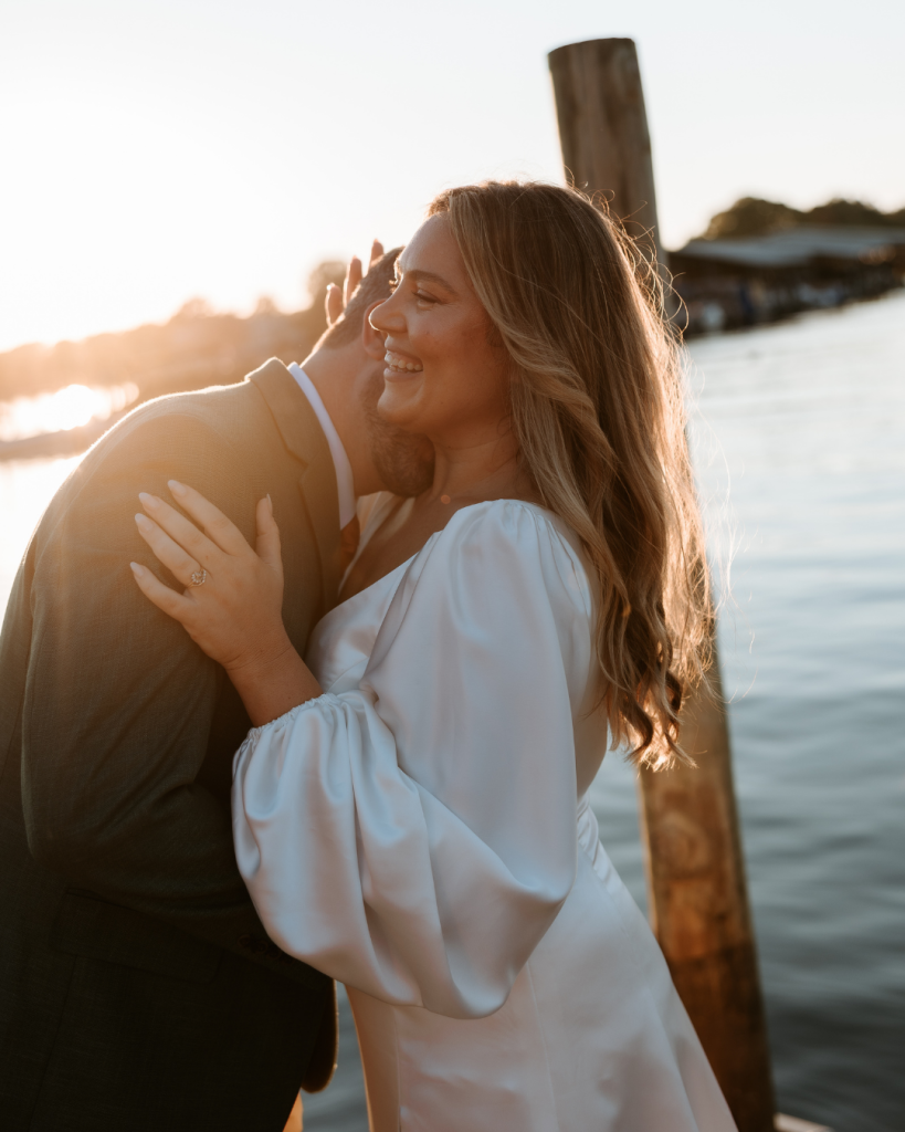 The couple embracing by the water at sunset, bathed in warm golden light.