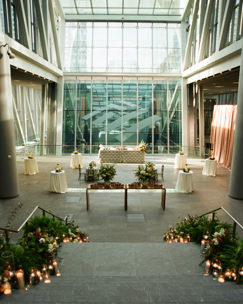 Ceremony setup inside The Urban Garden at The Ritz Carlton Charlotte with aisle greenery, candles, and a modern indoor atrium backdrop