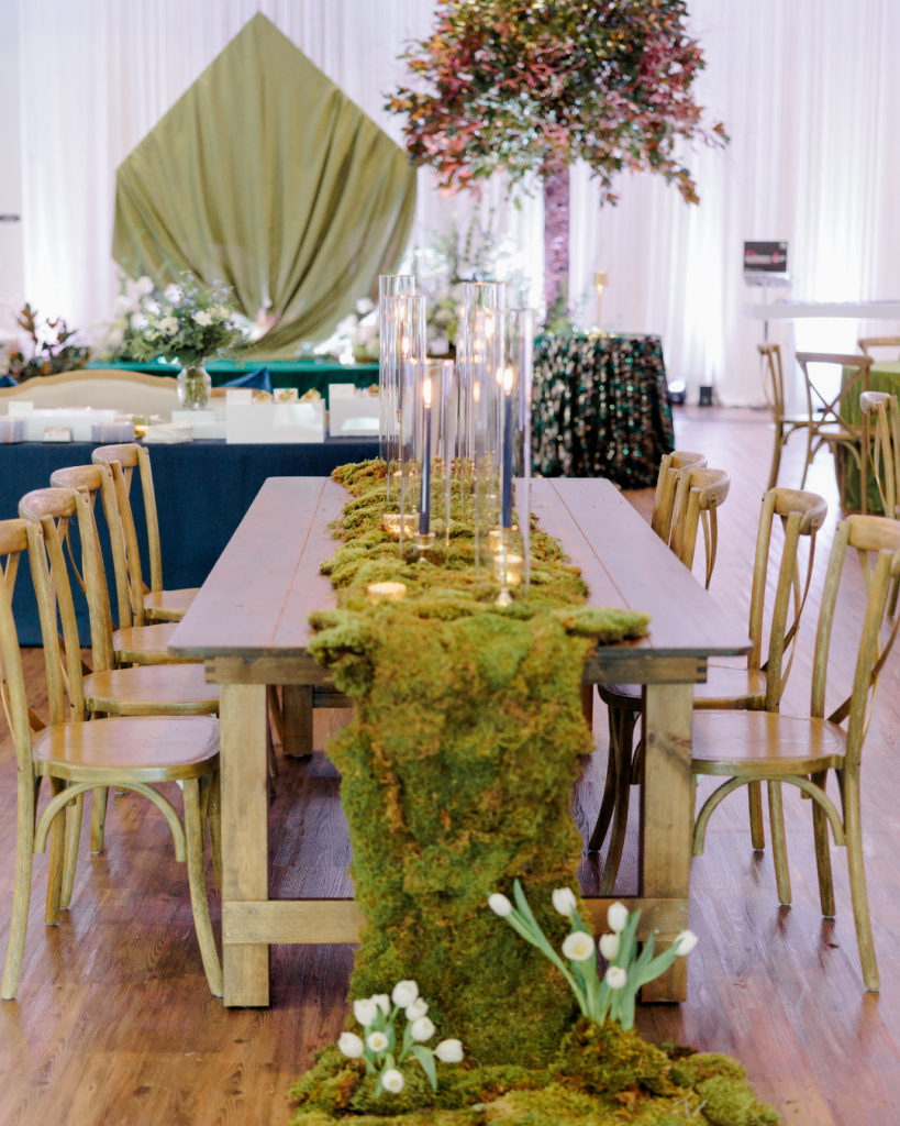 Long wooden reception table with cascading moss runner and glass cylinder candles styled by J. Starr’s Flower Barn at King Cole Farm barn venue in Dover, Delaware.