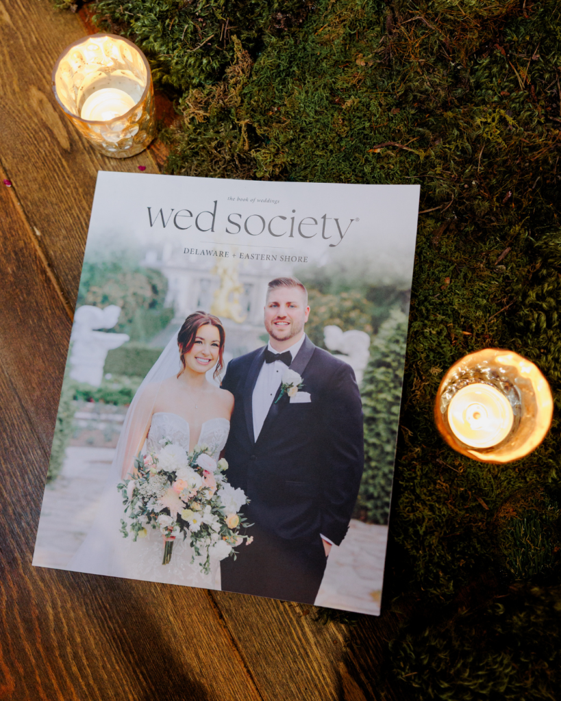 Wed Society Delaware + Eastern Shore Book of Weddings magazine sitting on wood table with moss and candle light