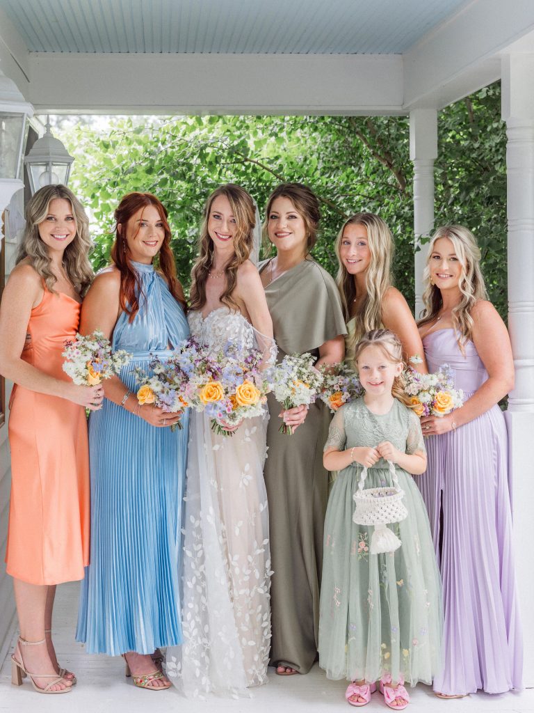 A bride posing with her bridesmaids and flower girl in a mix of colorful pastel dresses, photographed by Love Tree Studios.