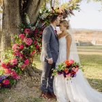 Bride and Groom posing in front of tree with colorful flowers set up around