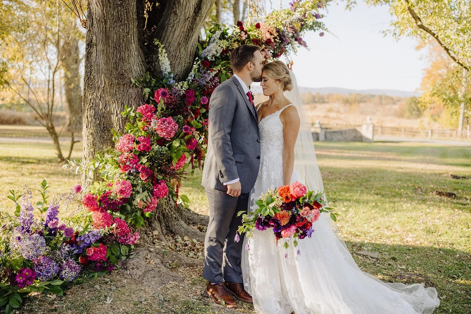 Bride and Groom posing in front of tree with colorful flowers set up around