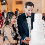 Couple cutting white four tier wedding cake at wedding reception