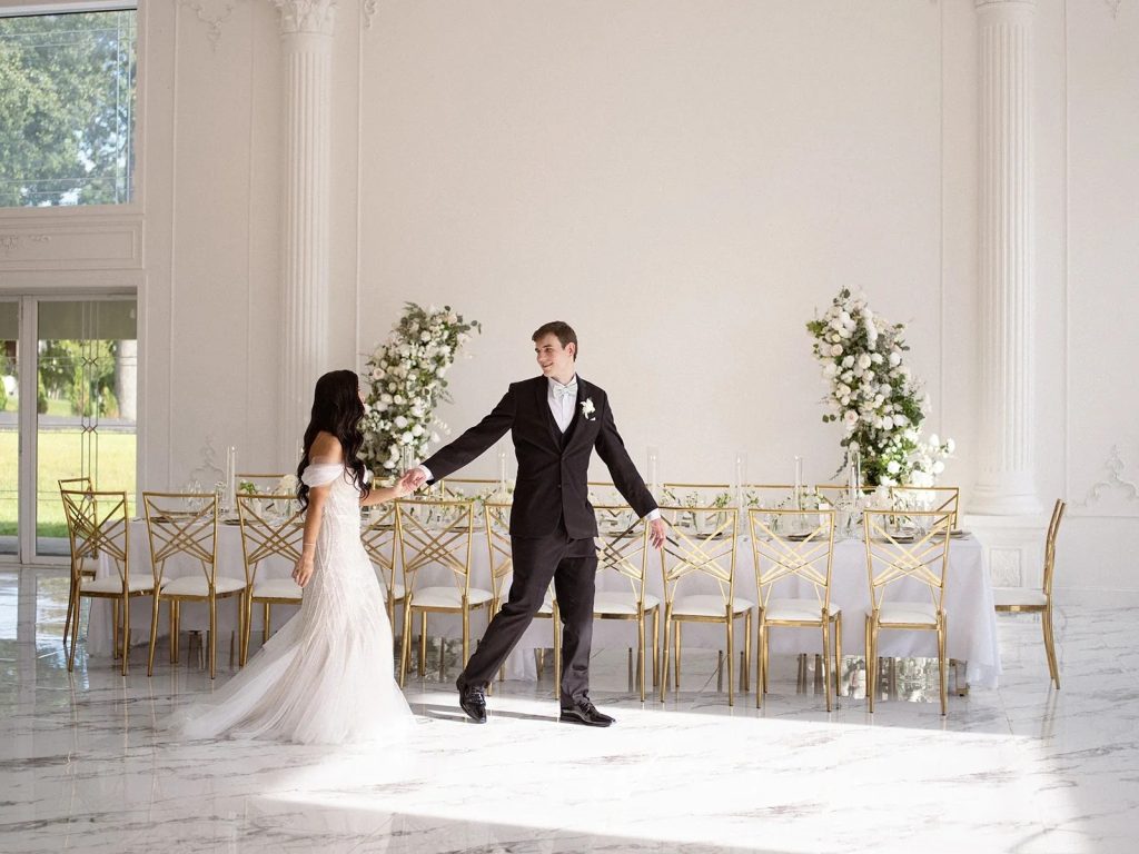 husband and wife walking through all white indoor wedding reception area for the first time