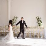 husband and wife walking through all white indoor wedding reception area for the first time