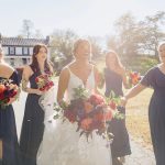 Bride and Bridesmaids walking to outdoor ceremony space with their deep red flowers