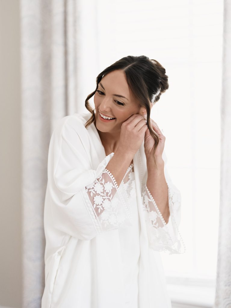 bride putting on jewelry after her hair and makeup are complete during wedding morning