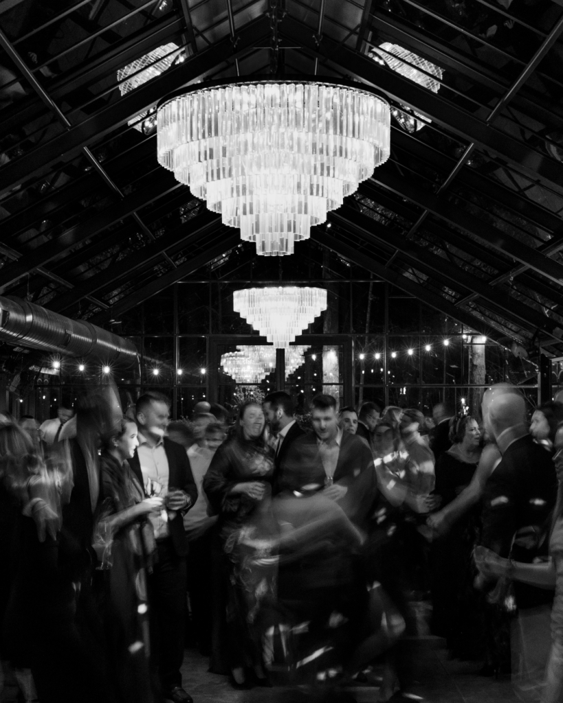Black and white reception dance floor scene under chandeliers with guests celebrating and dancing