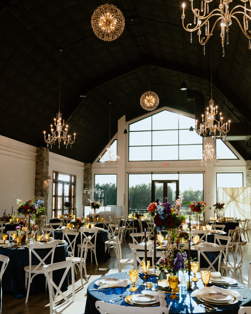 Elegant reception space with long tables, chandeliers, candlelight, and colorful floral centerpieces.