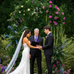 bride and goom at the alter with a colorful floral arch and lots of greenery