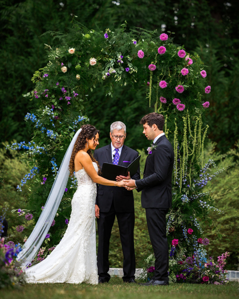 bride and goom at the alter with a colorful floral arch and lots of greenery