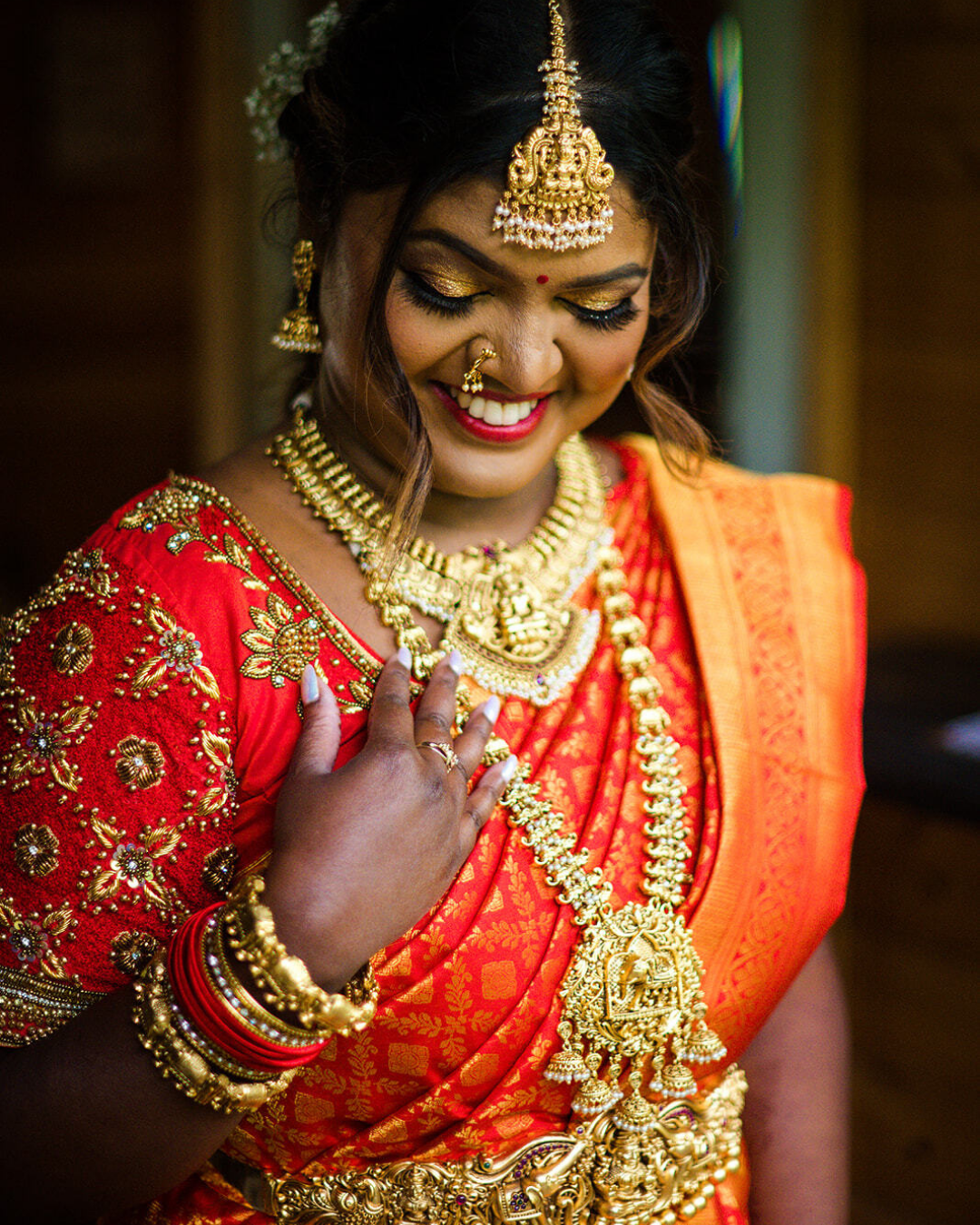 inidan bride in a vibrant orange dress with gold jewelry