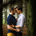 LGBTQ+ couple standing forehead to forehead with forest in background