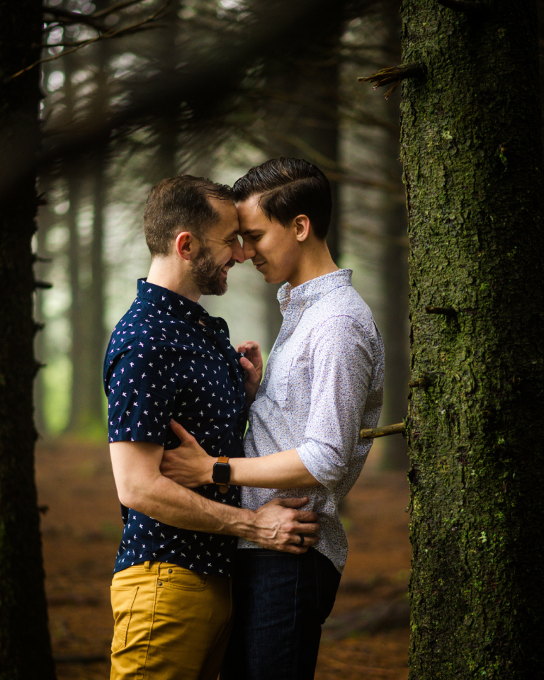 LGBTQ+ couple standing forehead to forehead with forest in background
