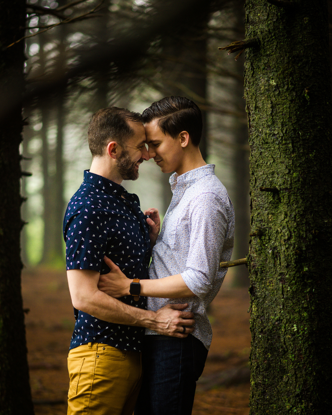 LGBTQ+ couple standing forehead to forehead with forest in background