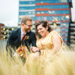 bride and groom in a grass field with a city view behind them smiling and laughing