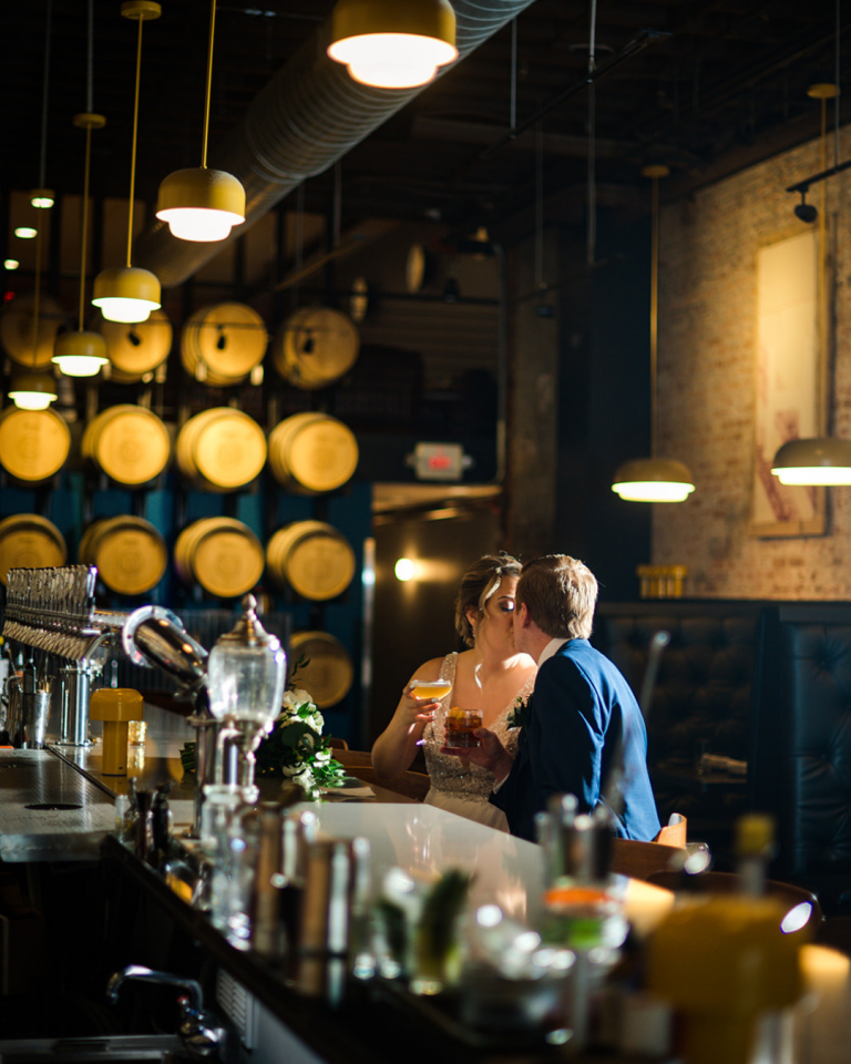 bride and groom kissing in a bar with whisky barrels behind them