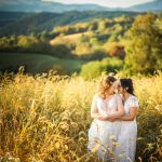 LGBTQ+ couple looking into eachothers eyes in their white bridal dresses with a beautiful mountain view behind them