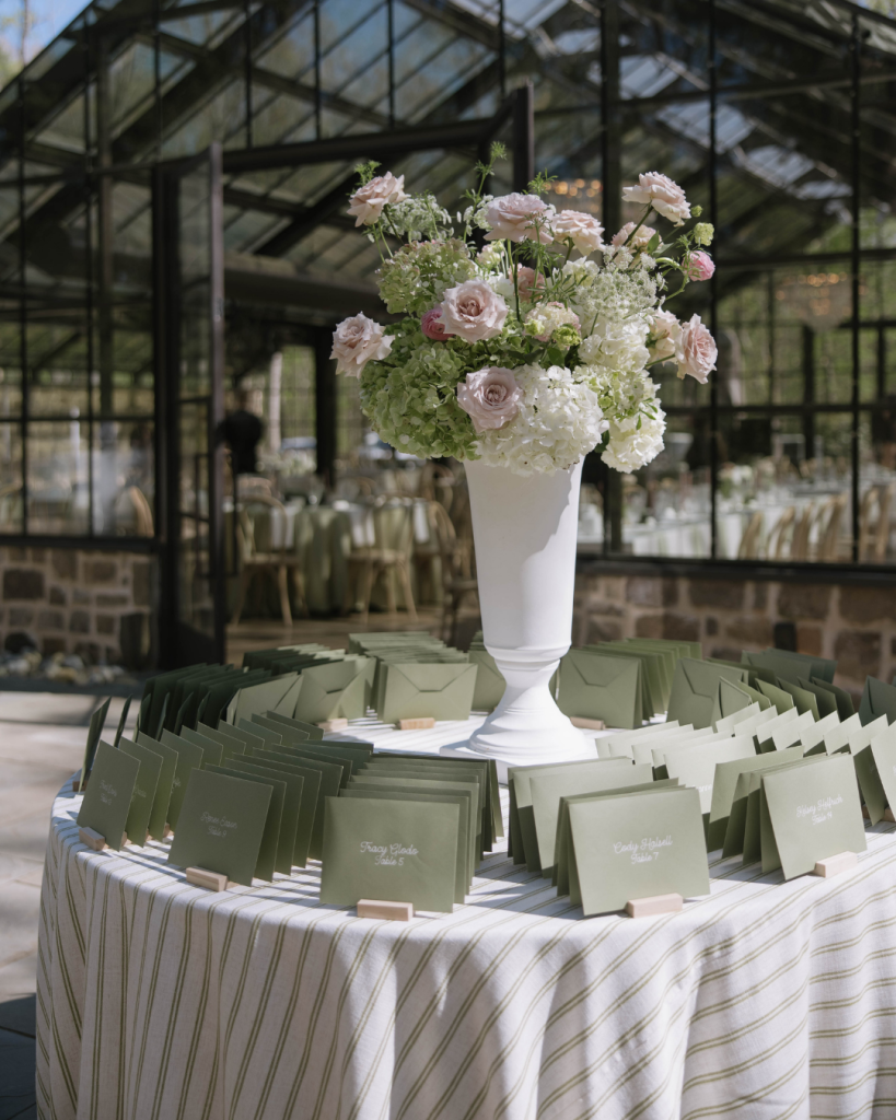 Escort card display with green envelopes and a tall floral arrangement on a round table