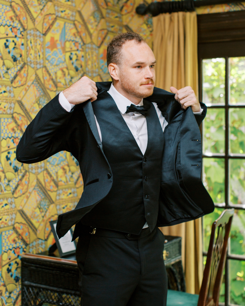 Groom adjusting tuxedo in patterned room at The Morehead Inn Charlotte NC wedding day preparation