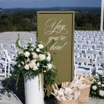 Ceremony welcome sign in outdoor wedding scene with white roses on column