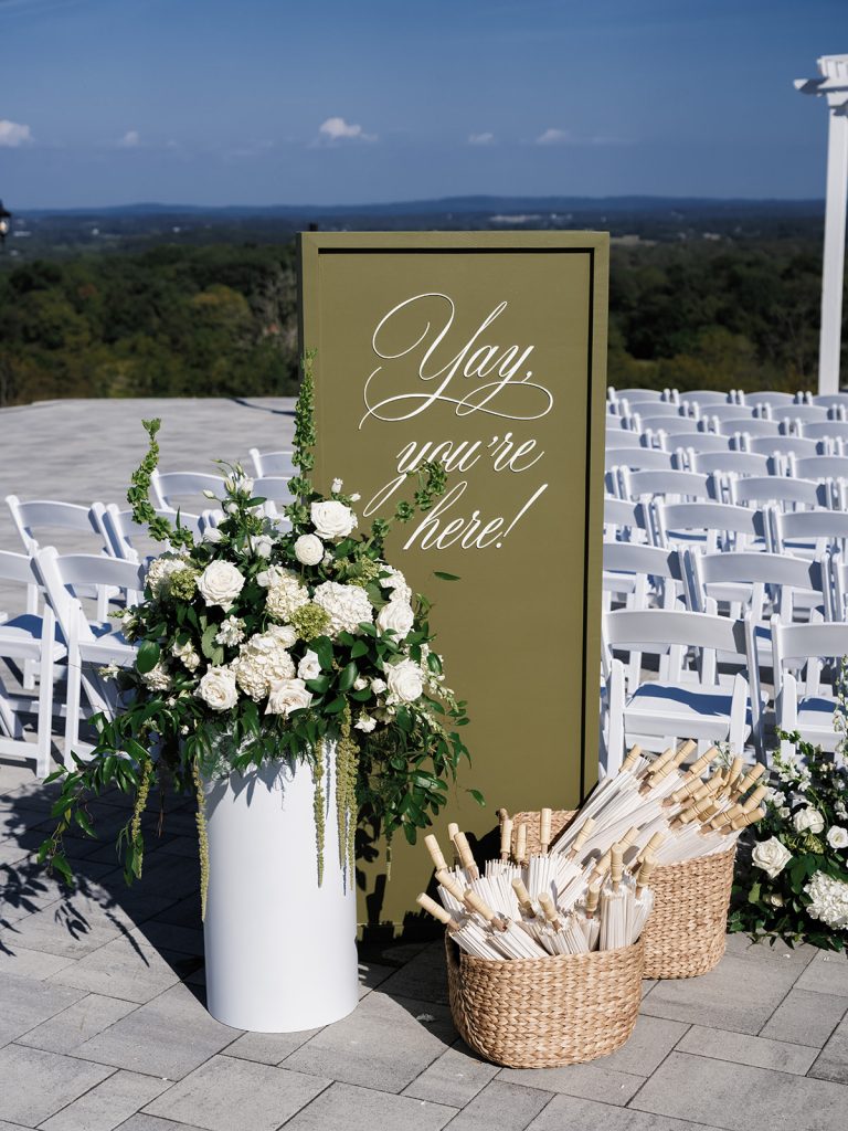 Ceremony welcome sign in outdoor wedding scene with white roses on column