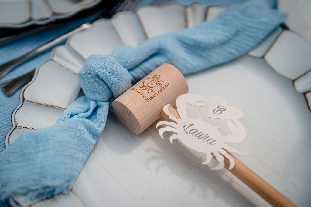Place setting with blue napkin, custom wooden mallet, and crab-shaped place card for coastal micro wedding at Addy Sea Historic Oceanfront Inn.