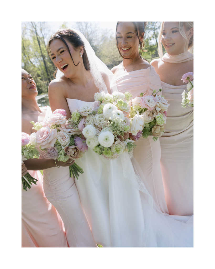 Bride with bridesmaids holding bouquets and smiling together in soft blush dresses