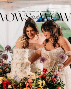 two brides cutting delicate detailed cake with wildflowers surrounding the cake