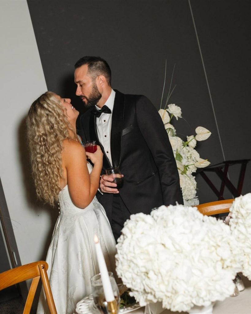 A bride and groom behind their sweat heart table adorned with white hydrangeas by Roses + Mint.