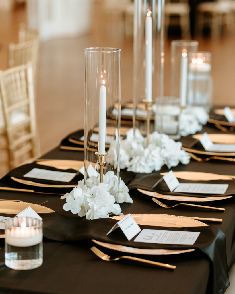 Close up of reception table décor with candles, black linens, and white floral arrangements