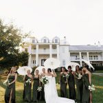 Bridesmaid and bride pose in front of mansion style wedding venue on green lawn