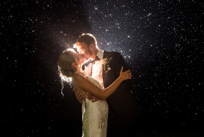 Bride and groom embracing under rain at night with dramatic backlighting during wedding portraits at Bear Trap Dunes in Ocean View, Delaware.
