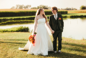 Bride and groom walking hand in hand along pond at golden hour during outdoor Eastern Shore Maryland farm wedding.