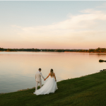 Bride and groom walking along a waterfront lawn on Maryland’s Eastern Shore at sunset, overlooking calm water and a scenic coastal landscape