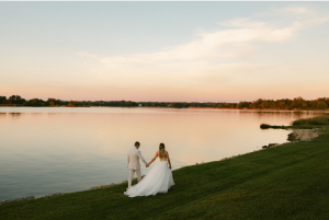 Bride and groom walking along a waterfront lawn on Maryland’s Eastern Shore at sunset, overlooking calm water and a scenic coastal landscape