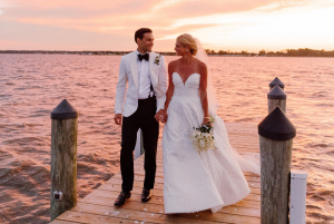 Bride and groom walking hand in hand along wooden dock during sunset portraits at coastal wedding in Rehoboth Beach, Delaware in August.