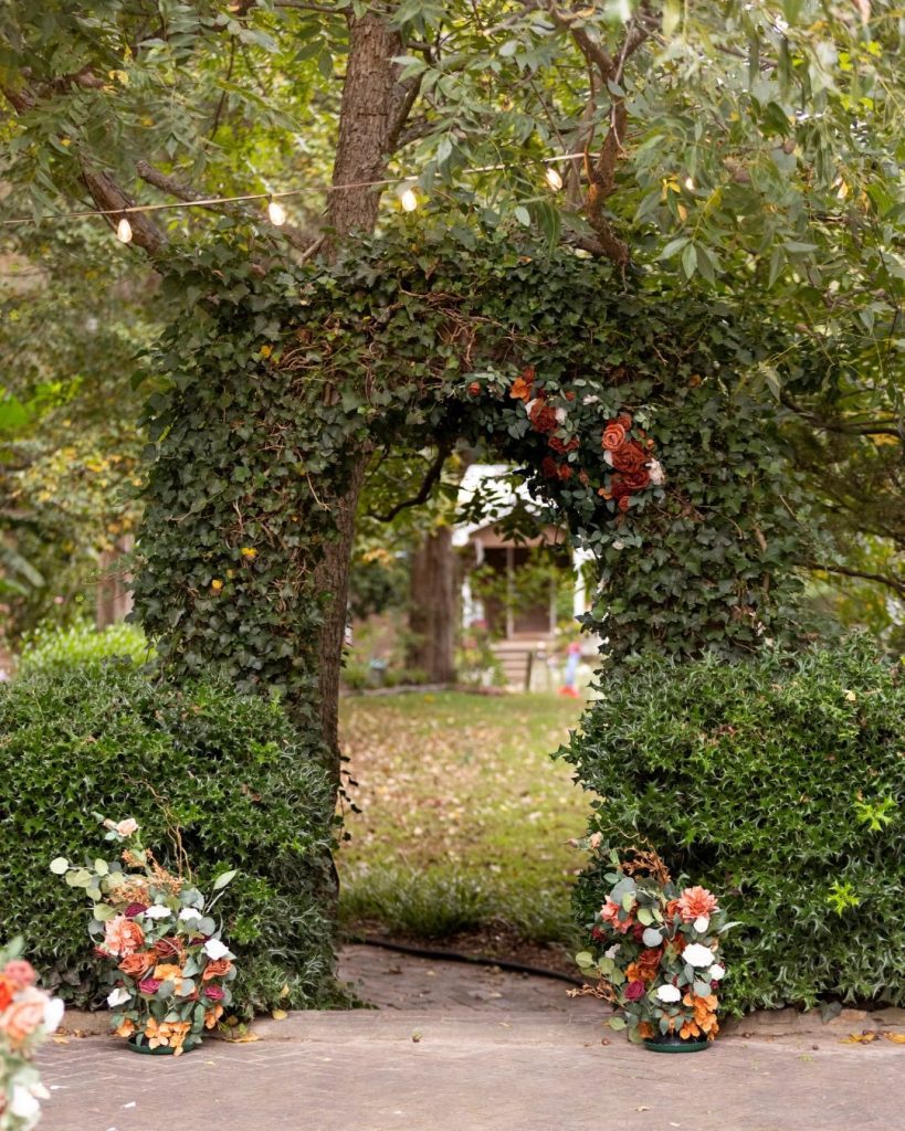 Ceremony arch with greenery and orange and red flowers