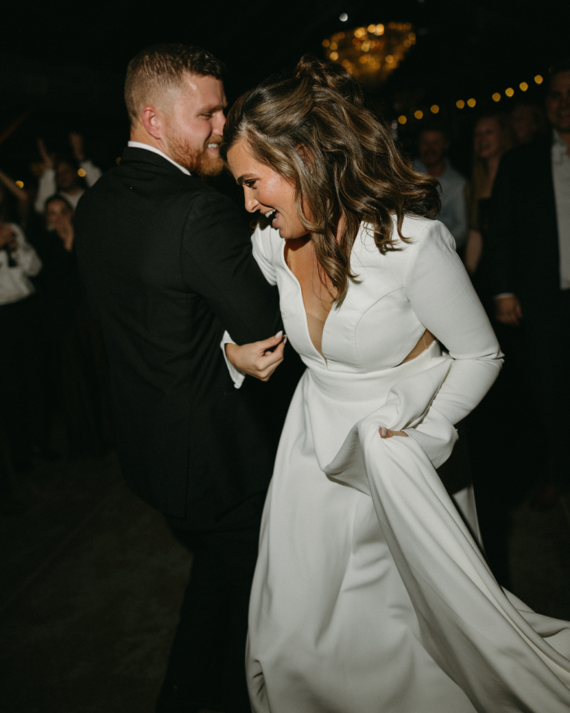 Bride and groom dancing together during the reception, surrounded by guests and soft evening lighting