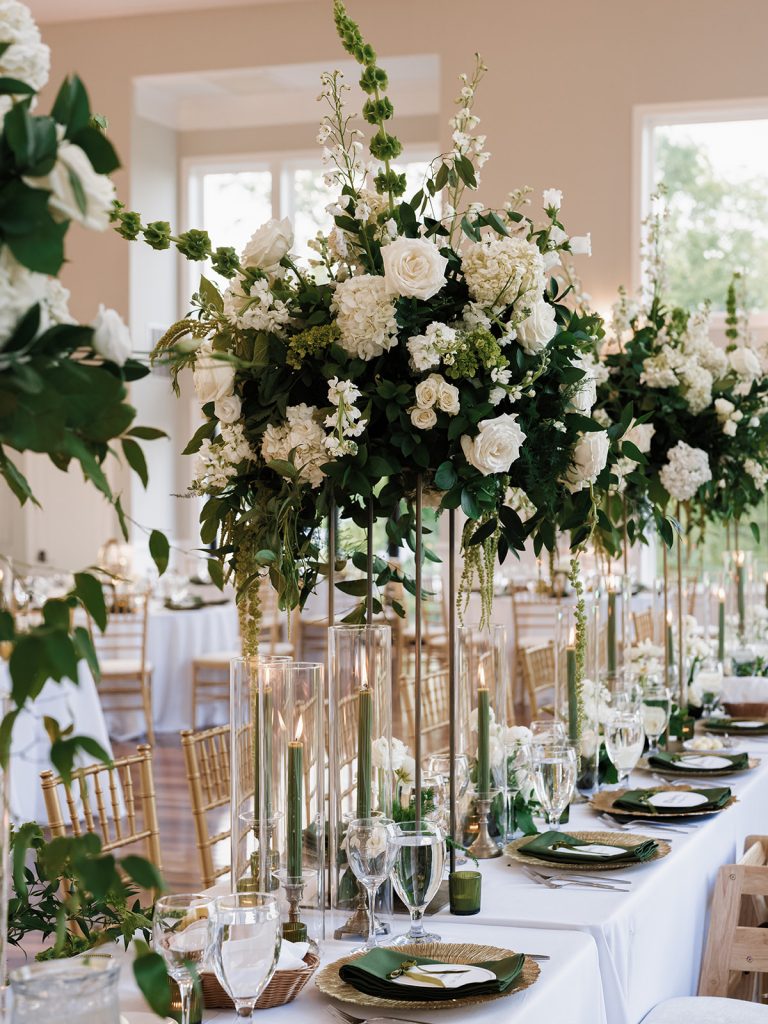 Close up details of tablescape at wedding reception featuring tall white roses vases on center table