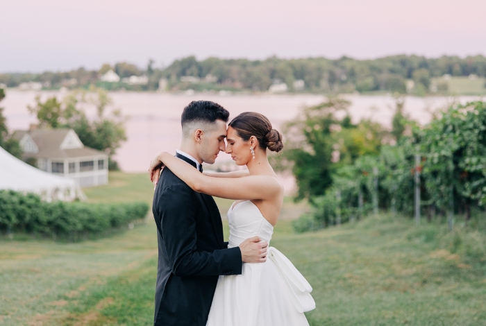 Bride and groom embracing on a hillside at Bohemia Overlook in Maryland, with vineyard rows and Elk River views in the background