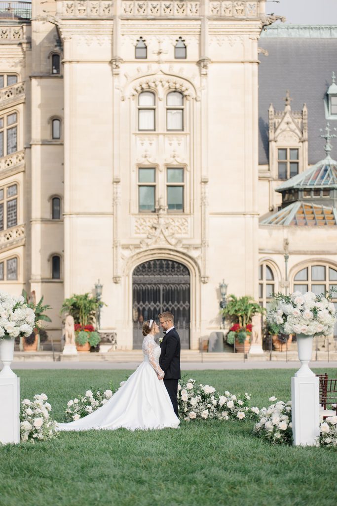 Bride and groom kissing in front of the Biltmore in north carolina with lush florals