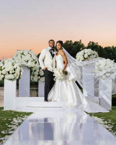Luxury wedding ceremony at Trump National Golf Course Charlotte featuring a bride and groom standing on a white stage surrounded by lush white floral arrangements and a reflective aisle
