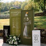 Large green installation of wedding seating chart with details like sconces and plexiglass