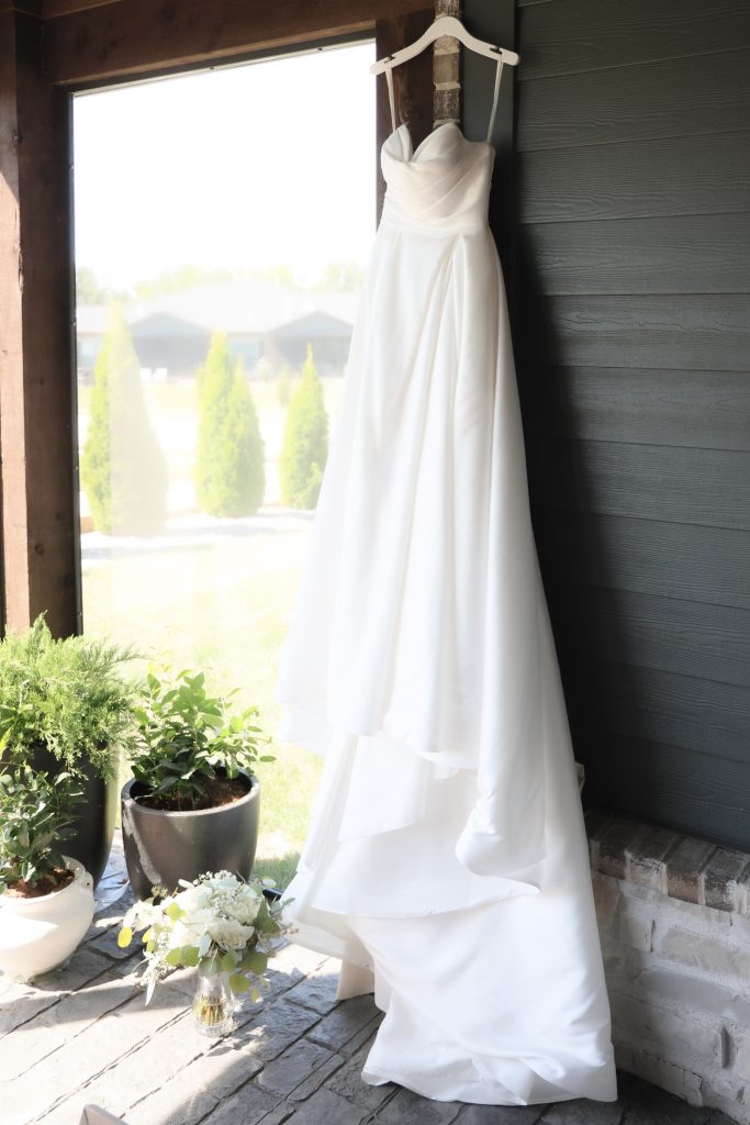 A Mia Grace Bridal gown hanging next to an orchard.